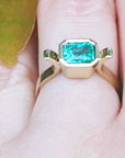 A yellow gold emerald ring held between fingers