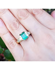 18K gold ring with a 2.10 ct rectangular emerald and bezel-set princess cut diamonds on a hand.