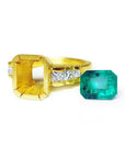 18K gold ring setting with bezel-set princess cut diamonds, beside a loose emerald-cut bluish-green emerald.
