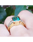 18K gold ring with a 2.10 ct emerald-cut bluish-green emerald and bezel-set princess-cut diamonds.