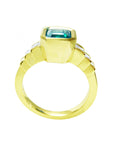 This bezel set emerald ring with accent princess cut diamonds is displaying its high top and lateral gallery.