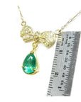 18K yellow gold bow-tie necklace with pave diamonds and a dangling pear-shaped emerald.