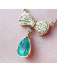 18K yellow gold bow-tie necklace with pave diamonds and a dangling pear-shaped Colombian emerald.