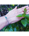 Hand wearing a bracelet with a genuine emerald against a natural background.