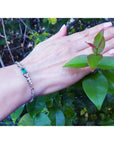 14K white gold bracelet with a rectangular Muzo Colombian emerald and six diamond accents on a woman's wrist.