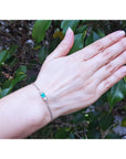 Woman's and wearing a bracelet with a natural emerald against a leafy background.