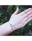 14K white gold bracelet with a sparkling emerald-cut Colombian emerald and diamonds on a woman's wrist.