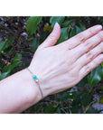 14K white gold bracelet with a sparkling emerald-cut Colombian emerald and diamonds on a woman's wrist.
