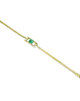 A distan view of a yellow gold bracelet with a Muzo emerald on a topside position.