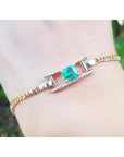 A 14k gold bracelet for women with a square natural emerald and diamonds displaying a vibrant medium-deep green color.
