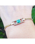 14K yellow gold bracelet with a central emerald-cut Colombian emerald and diamond accents on a curb chain.