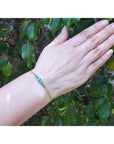 Women's 14K yellow gold bracelet with medium deep green Colombian emeralds on a wrist.