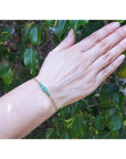 Women's 14K yellow gold bracelet with medium deep green Colombian emeralds on a wrist.