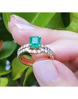 1.39 carat emerald bridal ring set with matching diamond band in 14K gold, held against green leaves.