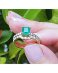 1.39 carat emerald bridal ring set with matching diamond band in 14K gold, held against green leaves.