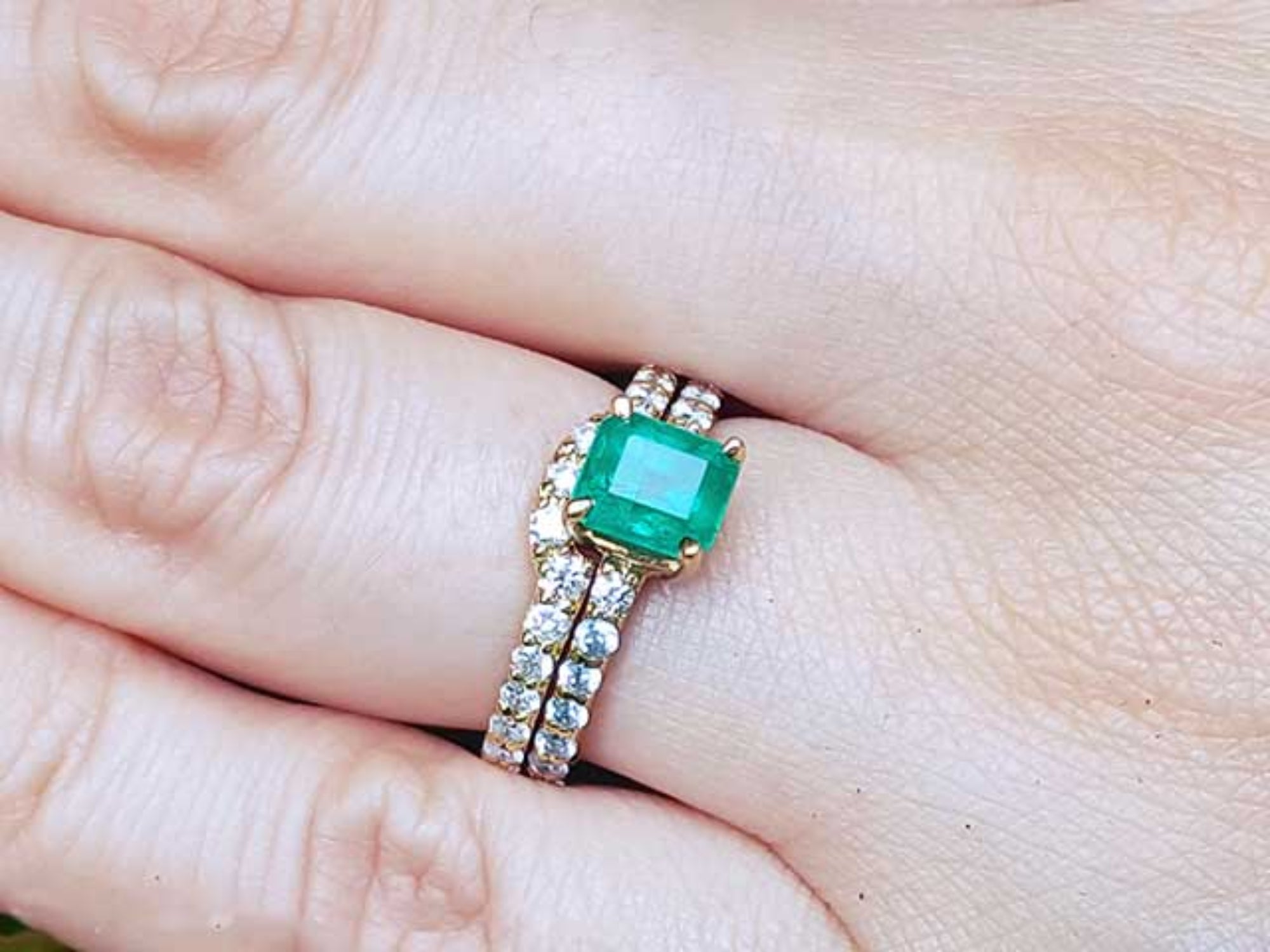A colombian emerald bridal ring with matching band set in yellow gold on a finger.