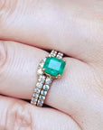A colombian emerald bridal ring with matching band set in yellow gold on a finger.