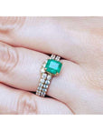 A colombian emerald bridal ring with matching band set in yellow gold on a finger.