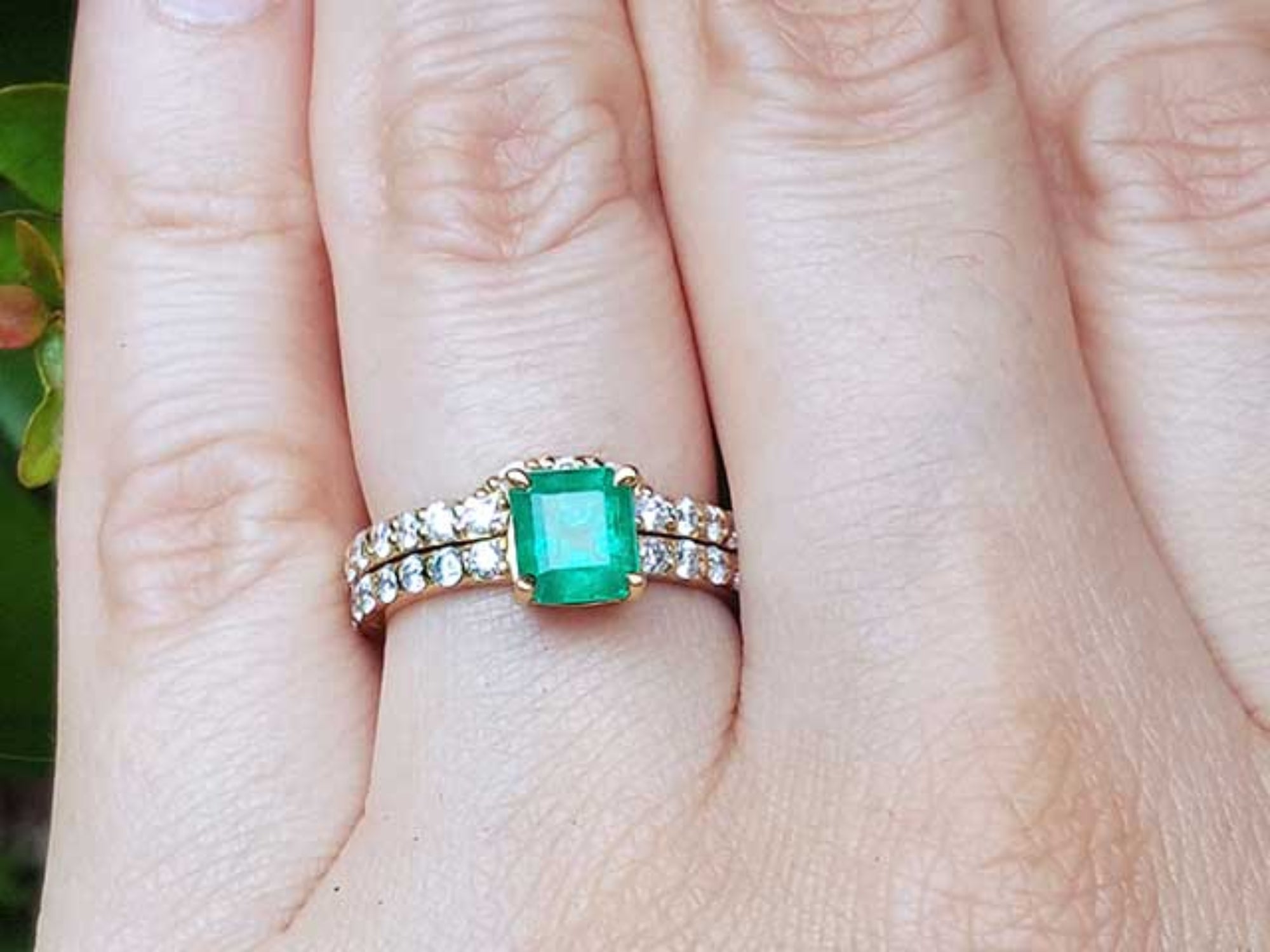 A natural emerald bridal ring with matching band set on a person's finger.