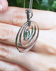 The back-side view of a circle of life emerald pendant held in a hand against a blurred natural background.