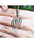 The back-side view of a circle of life emerald pendant held in a hand against a blurred natural background.