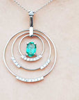 A triple circle of life pendant with an oval cut emerald on a light pink skin background.
