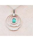 A triple circle of life pendant with an oval cut emerald on a light pink skin background.