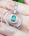 A white gold circle of life emerald pendant with diamonds held on a hand.