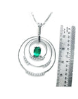 A triple circle of life natural emerald pendant next to a ruler for scale on a white background.