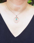 Necklace with three circles whit diamonds and in the enter an oval cut emerald worn by a woman against a natural background.