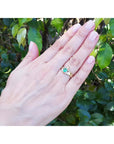 Hand wearing a 14k yellow gold emerald claddagh ring against a leafy background.