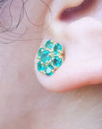 Close-up of an ear wearing a gold earring with natural emeralds.