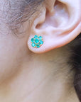 Close-up of a woman's ear wearing a emerald floral earring with blurred background