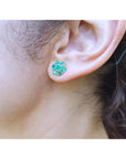 Close-up of a woman's ear wearing a emerald floral earring with blurred background