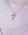 Necklace with a cross pendant featuring round natural emeralds worn on a person's neck.