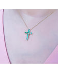 14K yellow gold cross pendant necklace with eleven round-cut Colombian emeralds on a woman's neck.