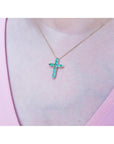 14K yellow gold cross pendant necklace with eleven round-cut Colombian emeralds on a woman's neck.