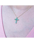 14K yellow gold cross pendant necklace with eleven round-cut Colombian emeralds on a woman's neck.