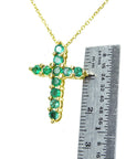 Natural emerald cross necklace next to a ruler on a white background.
