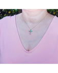 A woman wearing a pink top with a necklace featuring an emerald cross pendant.