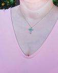 A woman wearing a pink top with a necklace featuring an emerald cross pendant.