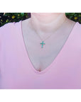 14K yellow gold cross pendant necklace with eleven round-cut Colombian emeralds on a woman's neck.