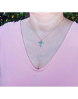 14K yellow gold cross pendant necklace with eleven round-cut Colombian emeralds on a woman's neck.