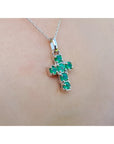 A 14k white gold cross pendant round cut natural colombian emeralds on a chain, worn on skin.