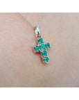 A 14k white gold cross pendant round cut natural colombian emeralds on a chain, worn on skin.