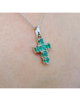 A 14k white gold cross pendant round cut natural colombian emeralds on a chain, worn on skin.