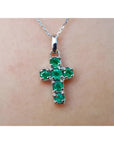 Cross-shaped natural emerald pendant on a chain, worn on skin.