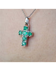 A 14k white gold genuine emerald cross pendant on a chain against a skin background.