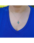A women wearing a blue shirt with a white gold necklace featuring a colombian emerald cross pendant.