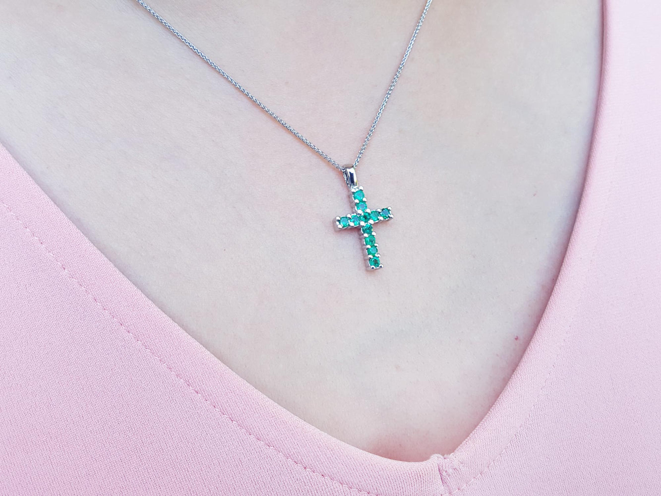Necklace with a cross emerald pendant featuring green round cut stones on a pink top.